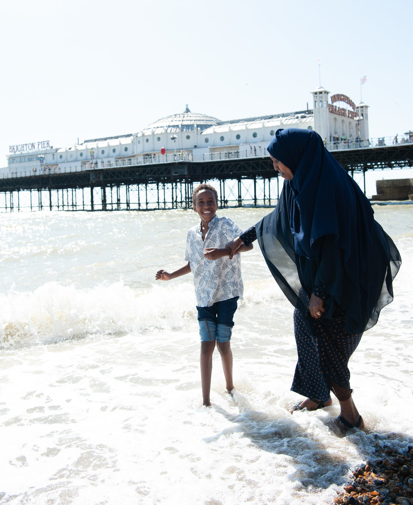 Adult and child paddling in sea, Brighton Pier in background