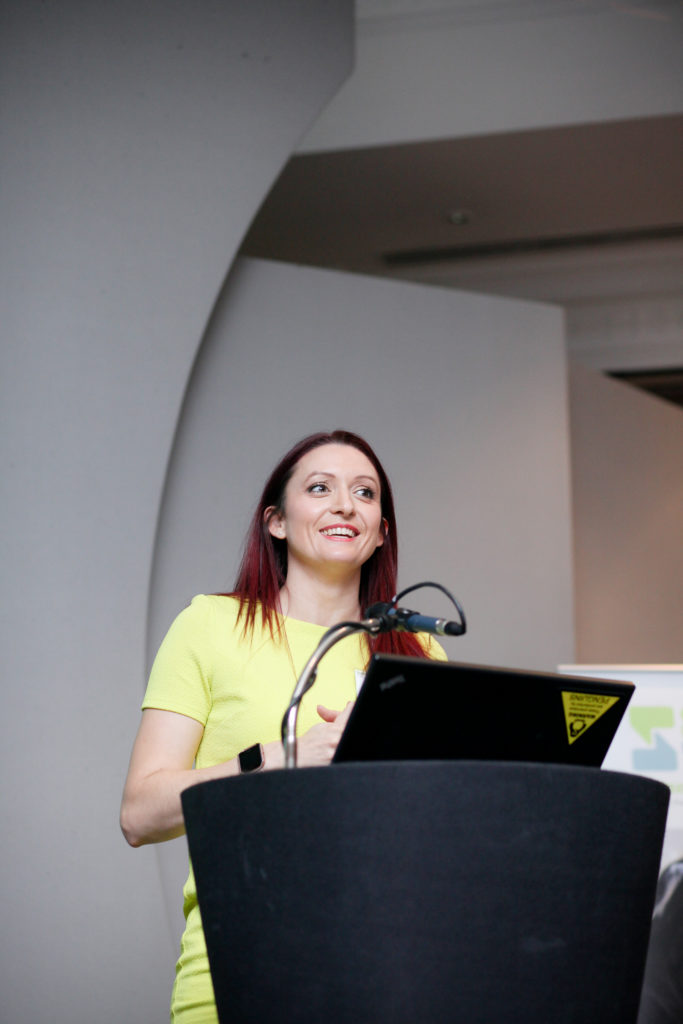 Speaker in yellow dress at event on stage with laptop