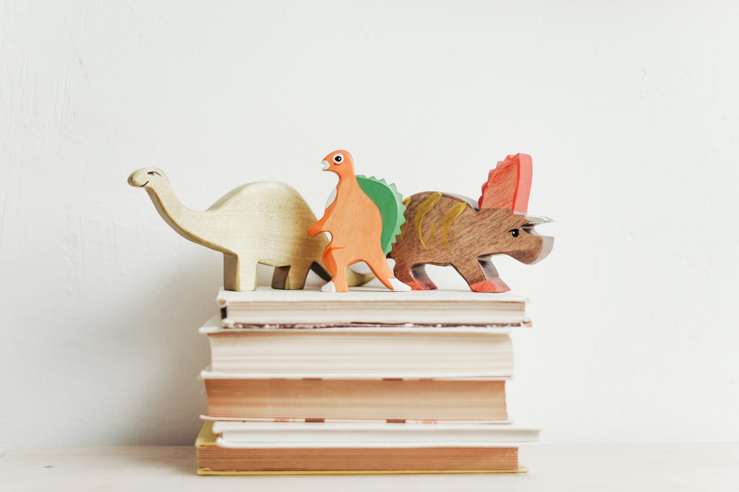 3 wooden dinosaur toys on stack of books