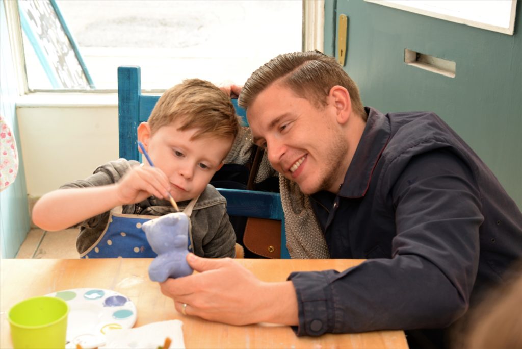 Dad and son at pottery class, son painting pottery