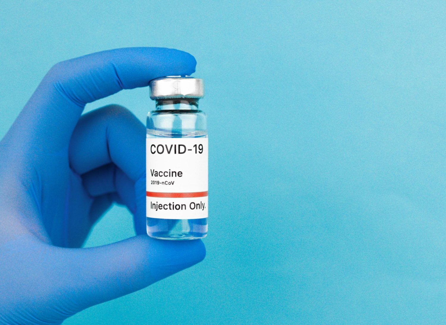 Gloved hand holding up a Covid vaccine vial