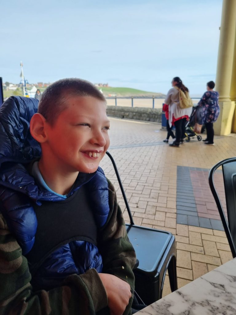 A child sitting outside at the seaside smiling.