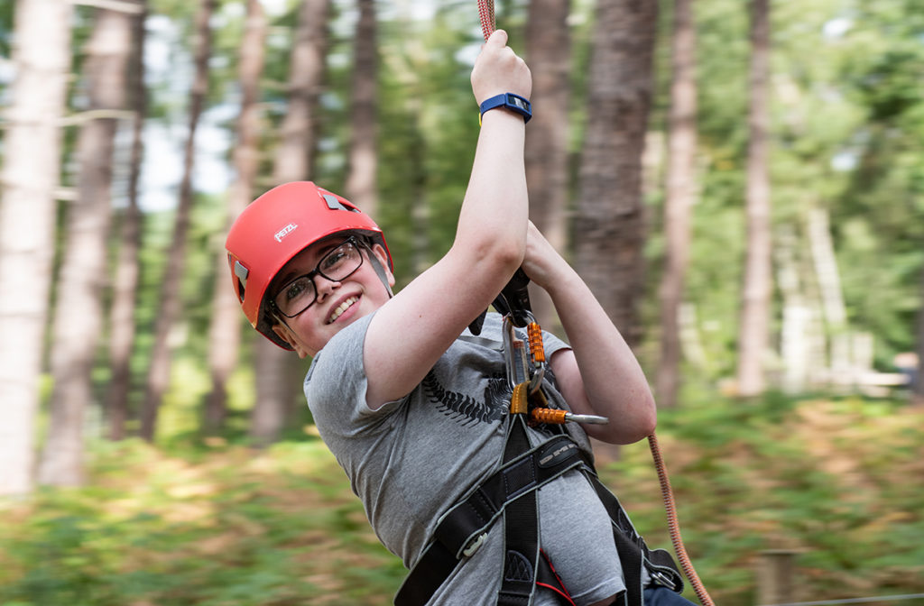 A child moving through the air on a zipline looking to camera