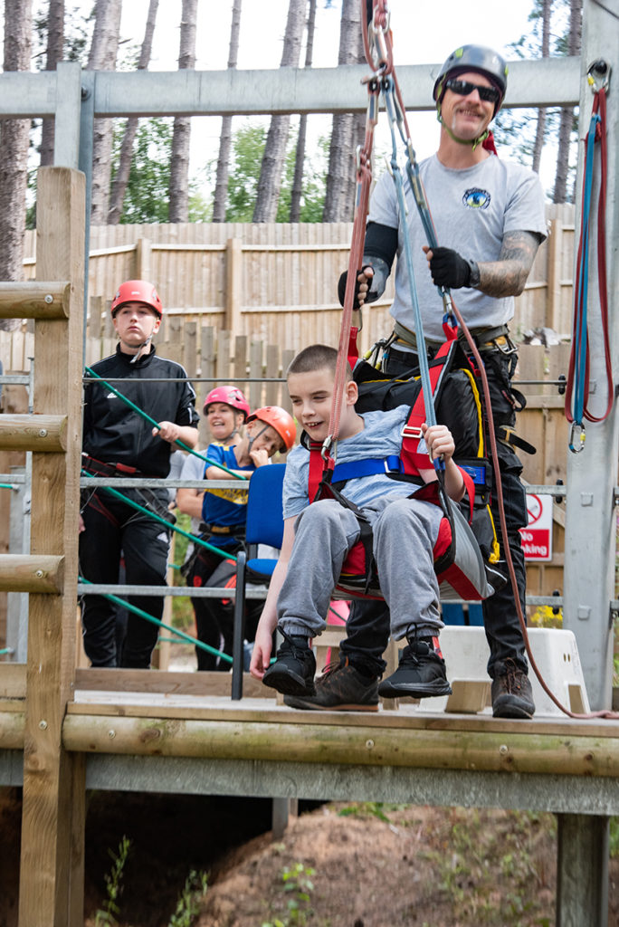 Child preparing for zipline with instructor at woodland adventure day