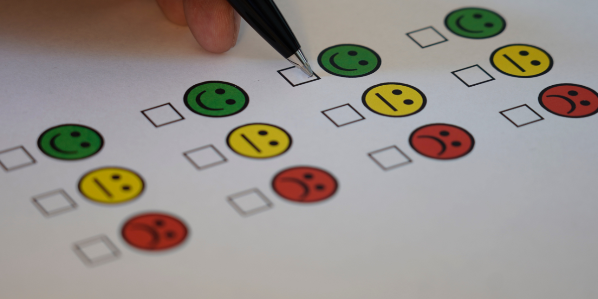 Hand holding pen hovering over a feedback survey with smiley faces next to tick boxes