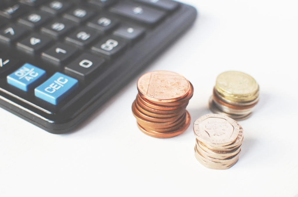 Three piles of coins on a desk next to calculator