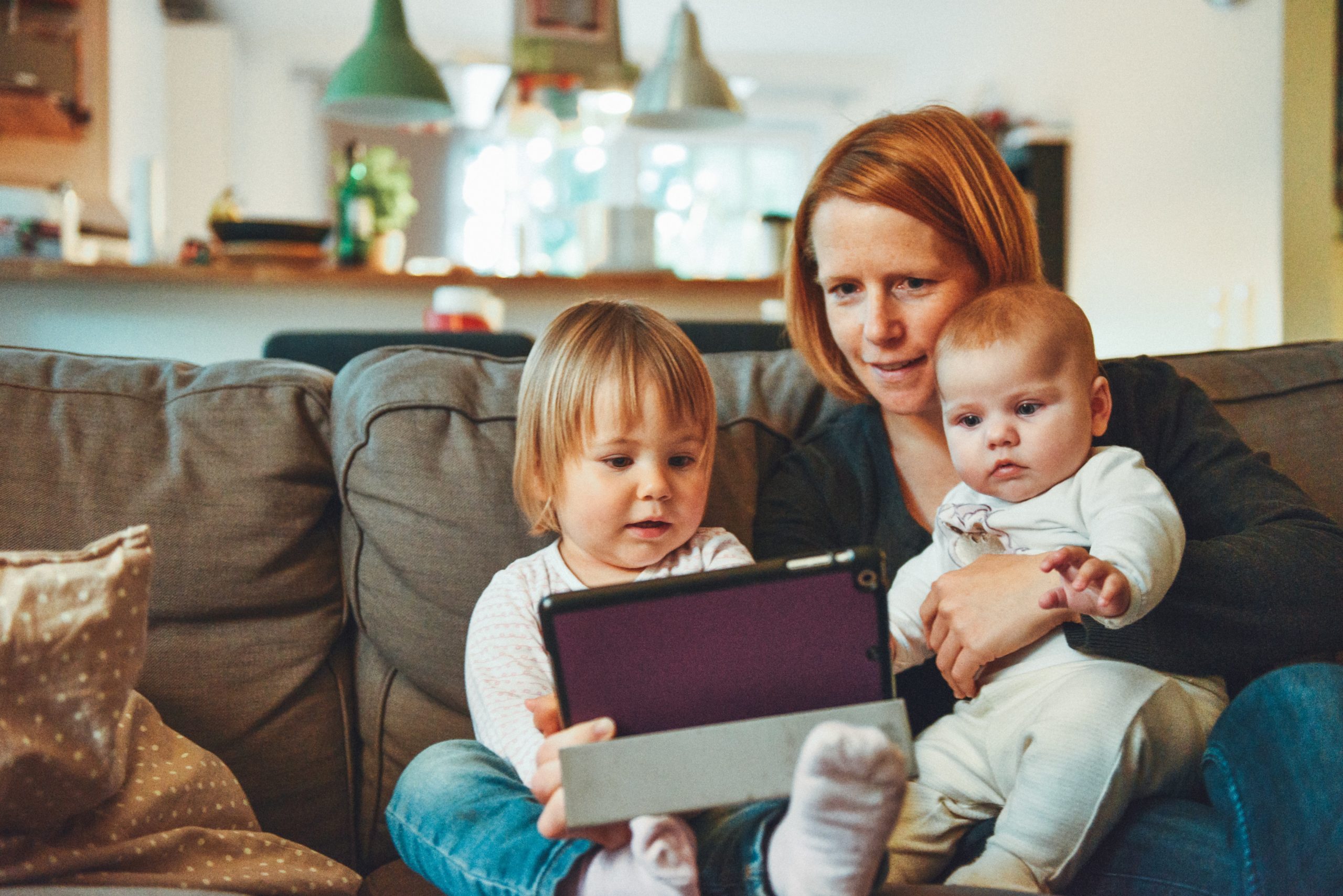 Parent with young child and baby looking at ipad on sofa