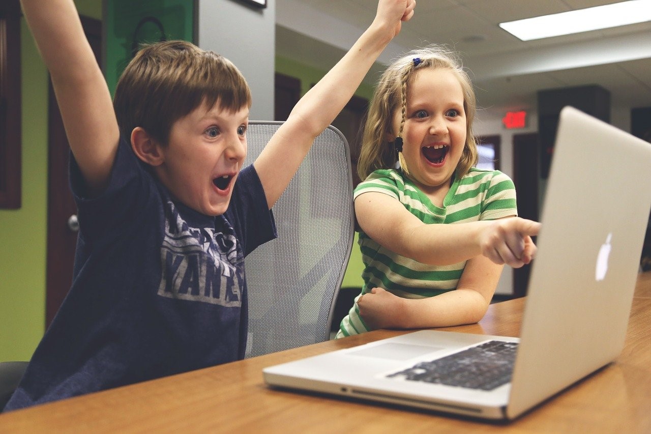 Two young children celebrating and pointing at laptop screen