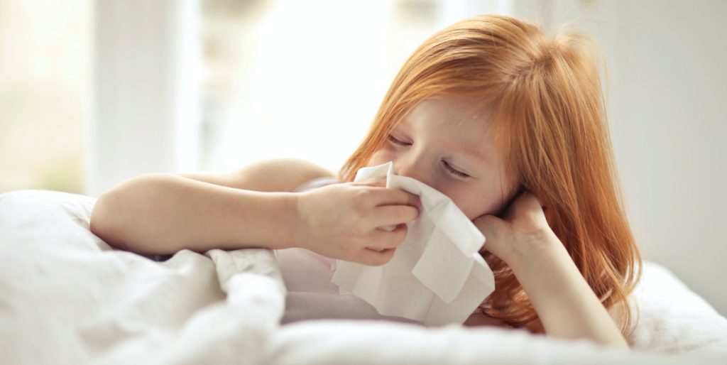 Child sneezing with a tissue in hand