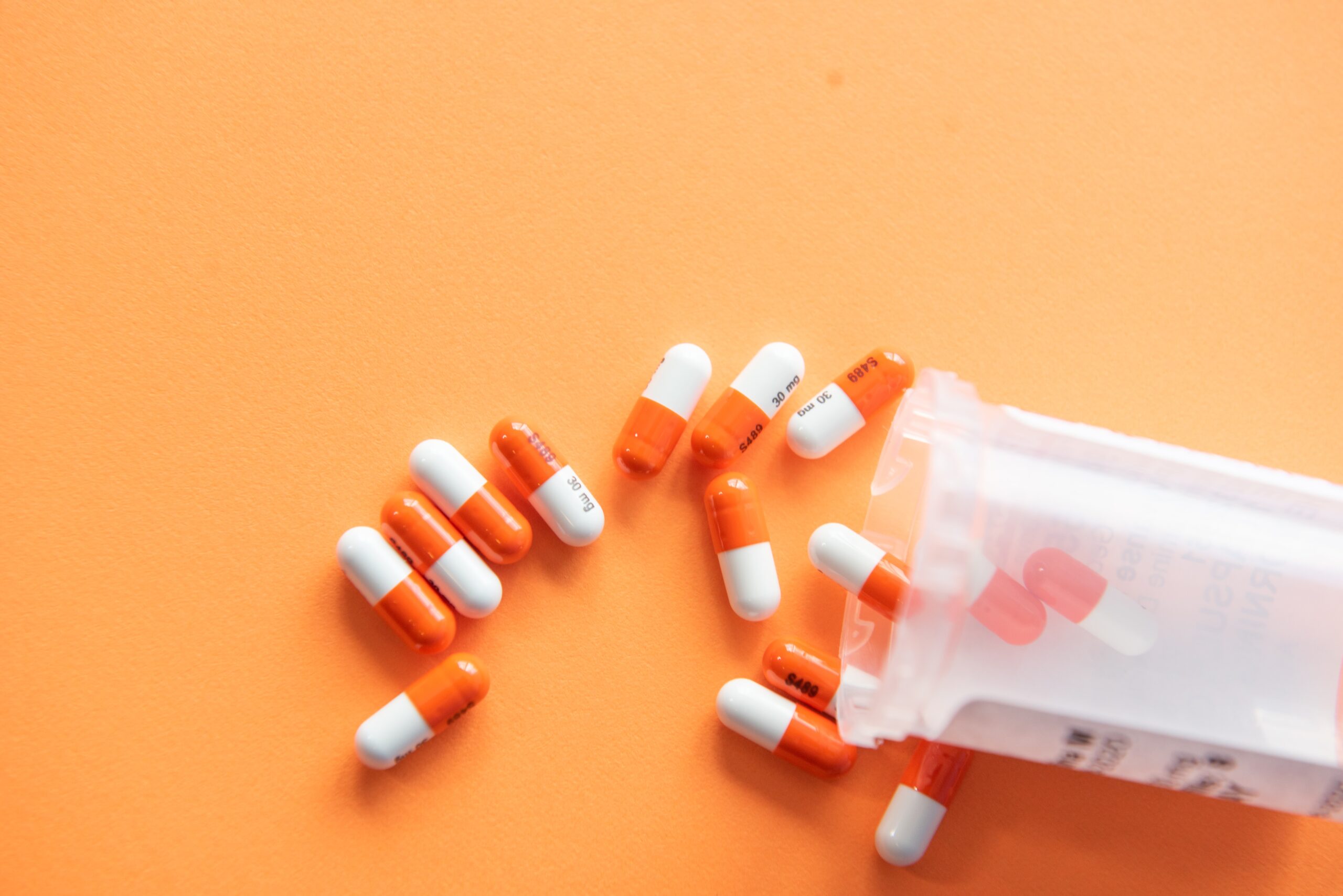 Pills spilling out of a bottle against an orange background