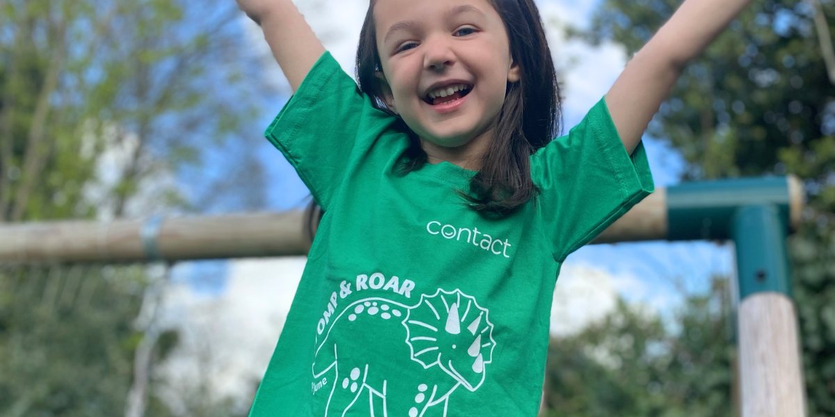 Child in a park jumping in the air wearing a green DinoDay t-shirt