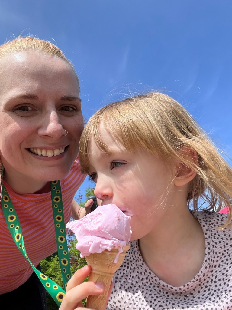 mum and daugther. Mum is smiling wearing a sunflower lanyard. Daughter is eating ice cream