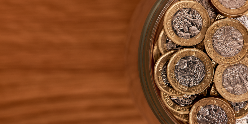 Top-down view of a jar on a wooden surface filled with British Pound coins .