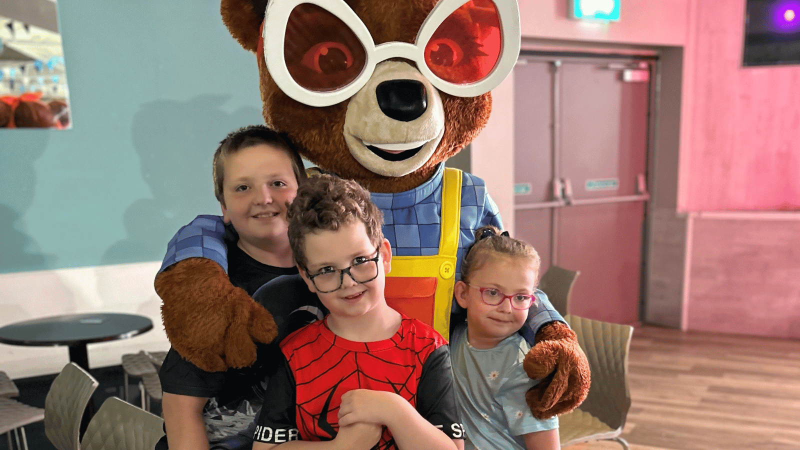 Three children standing with person in a cartoon squirrel costume