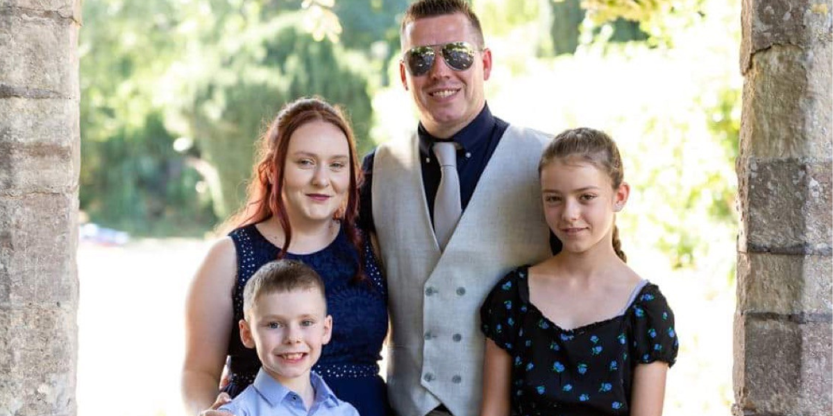 Lottery winner Sara stood with her partner and two children in a doorway, smiling and looking at the camera