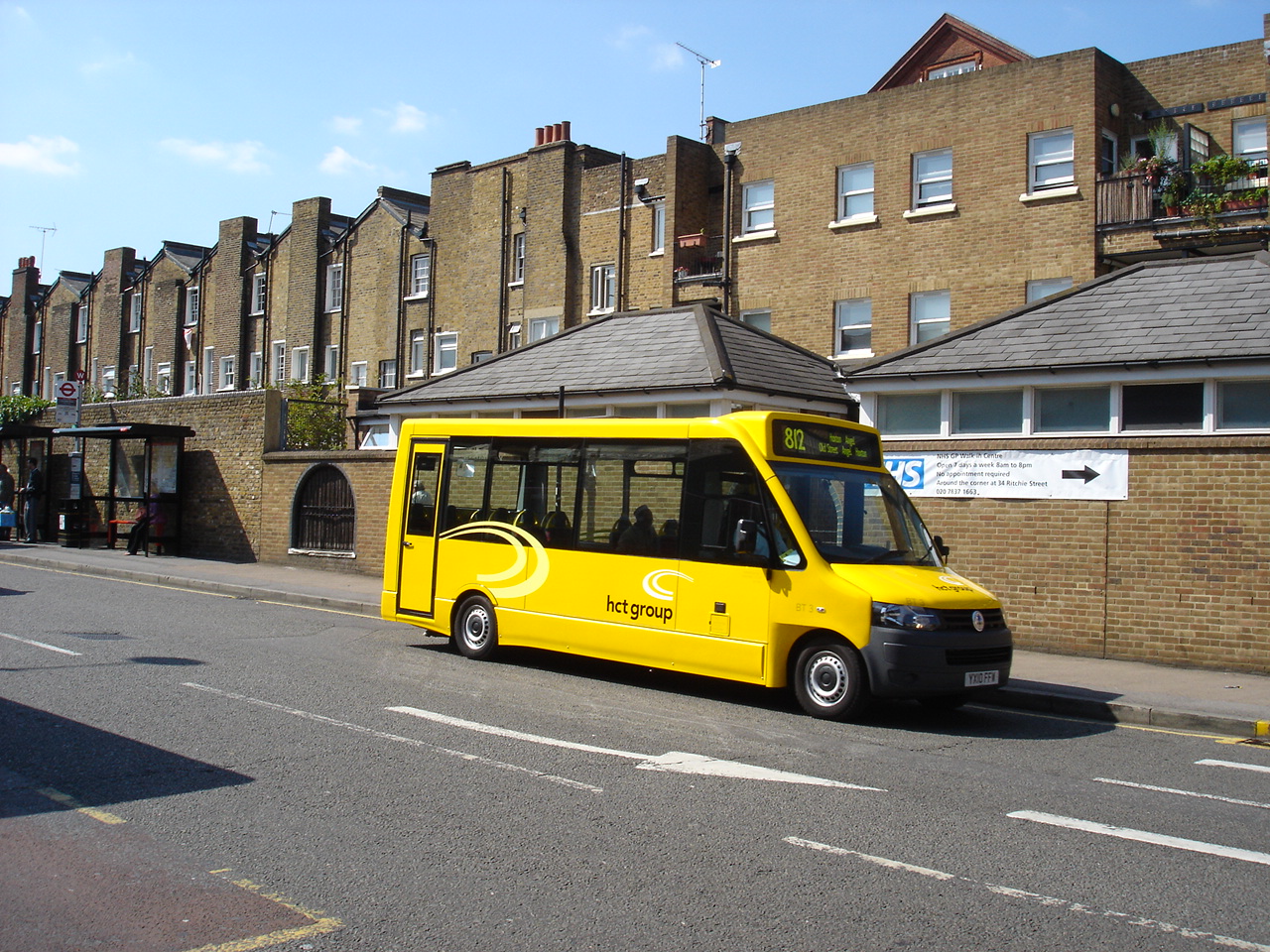 A yellow school minibus driving through suburban UK streets.