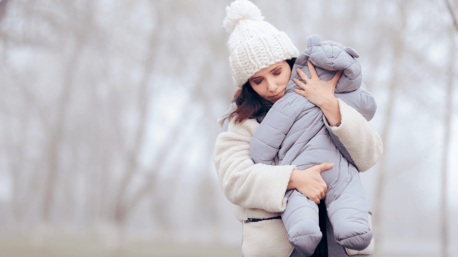 Mother holding baby in snowy cold weather with a concerned look on her face.
