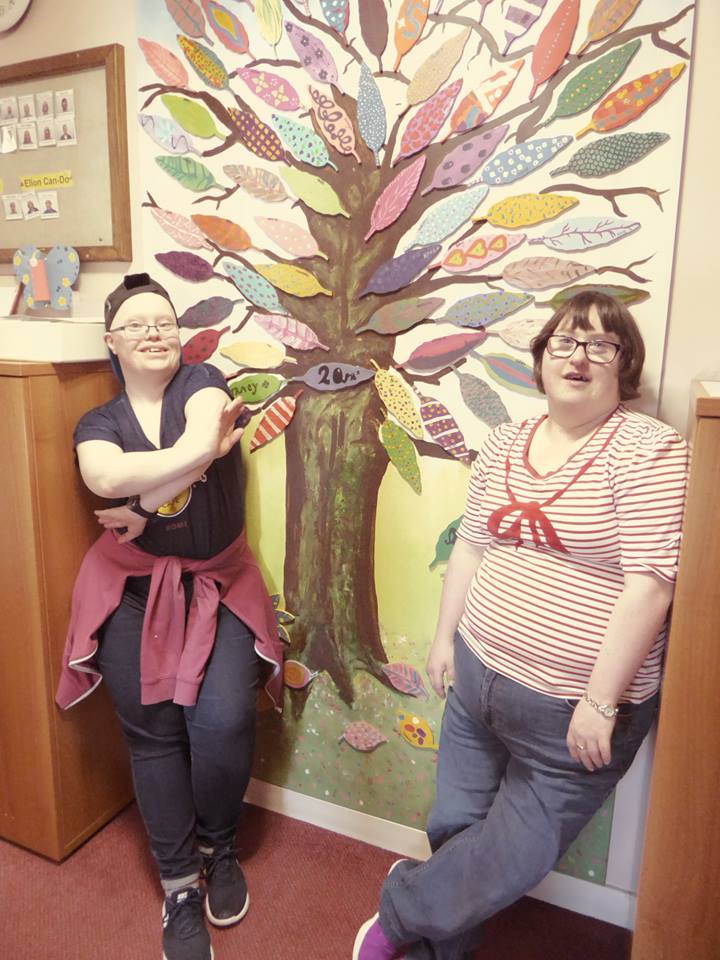 Two young people standing in front of a tree mural