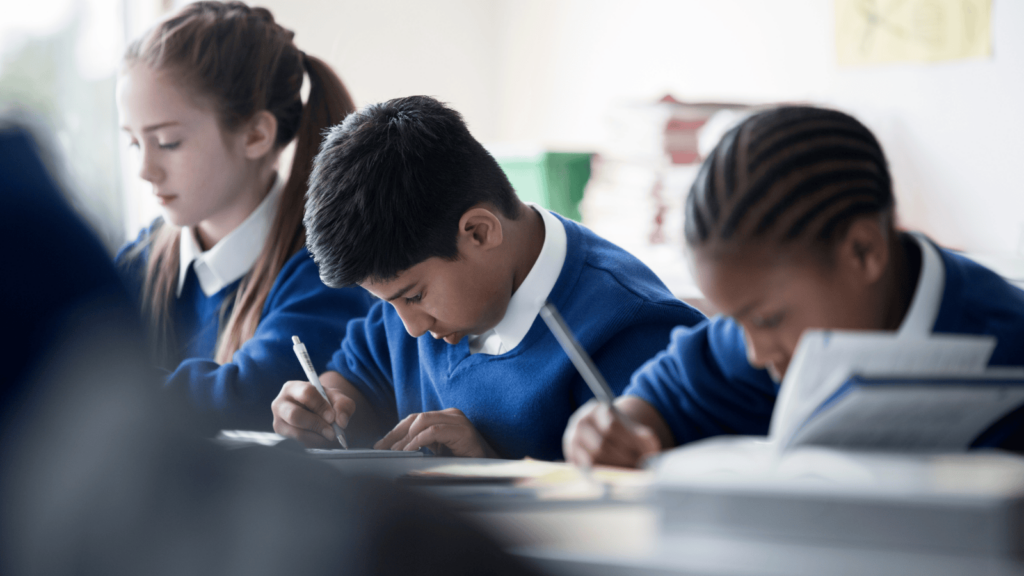 School children in a row at a desk writing with pencils