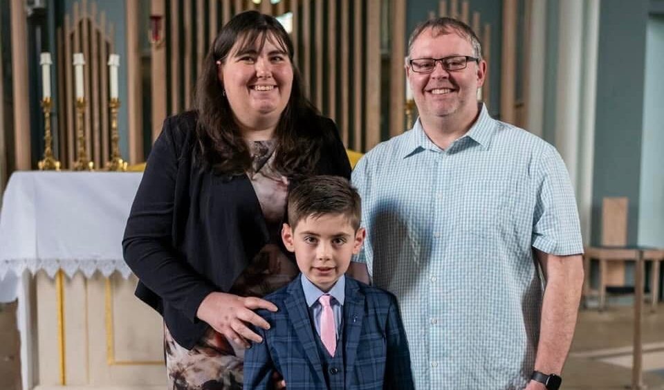 A young boy stands between his two parents, all looking at the camera.