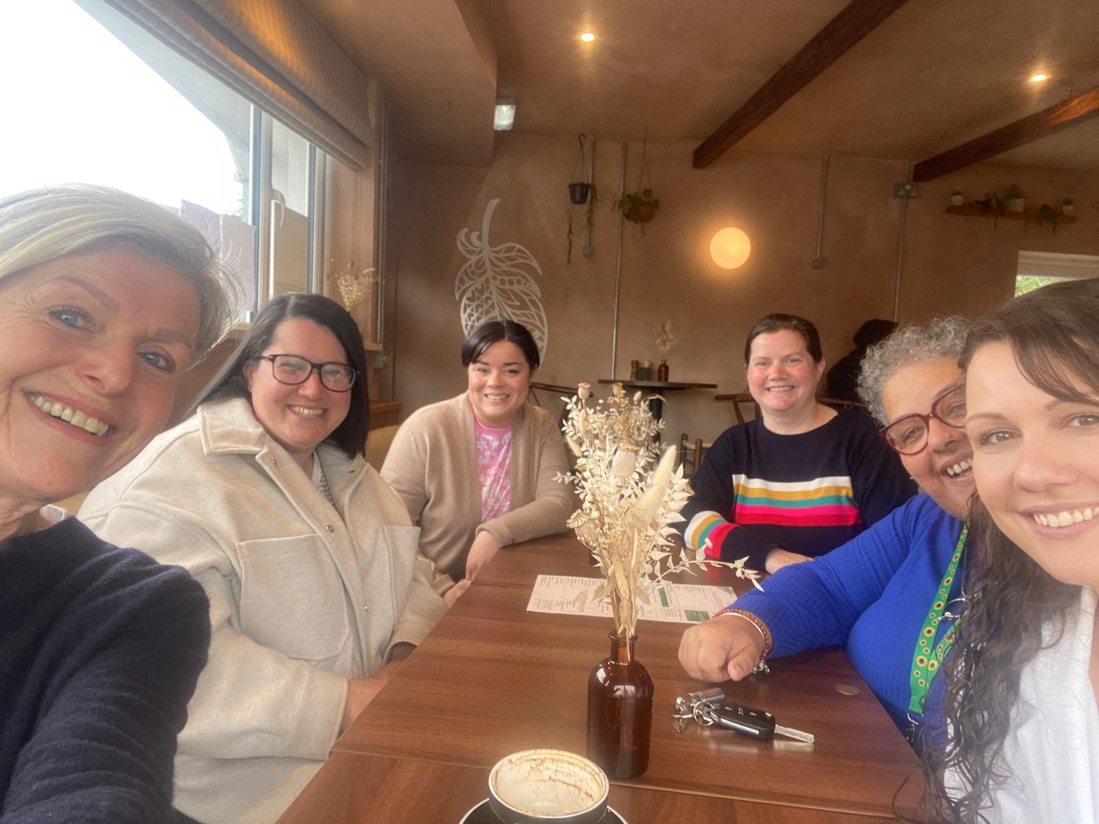 A group of women at a coffee get-together sitting around a table and smiling at the camera