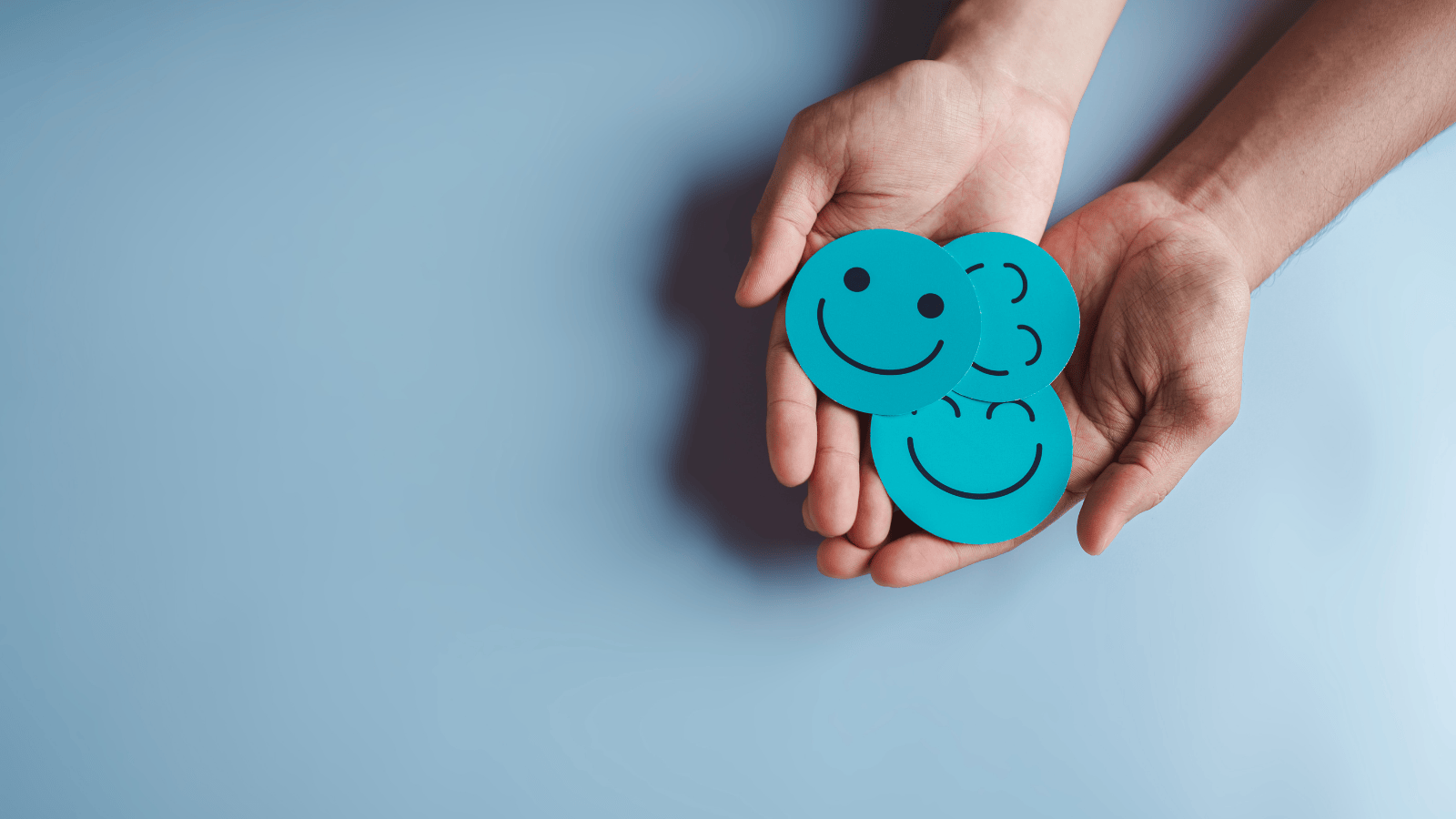 A pair of open hands holding blue circle smiley face badges