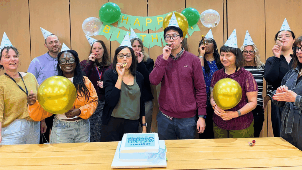 People from Contact in party hats, blowing whistles, with a party banner and cake