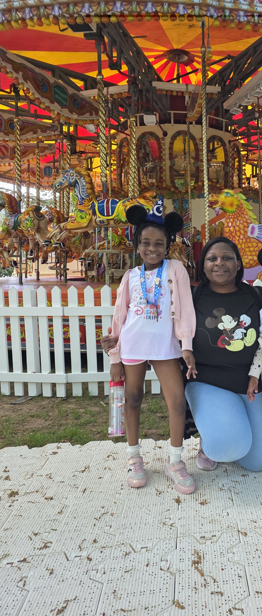 A mother and daughter standing in front of a fairground carousel
