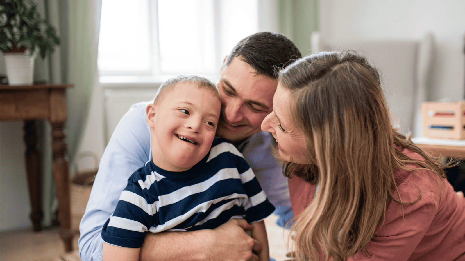 Two parents cuddling and smiling with pride at their child with Down Syndrome.