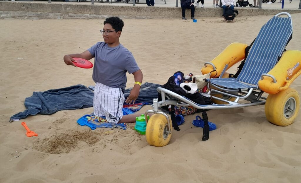 Boy playing on the beach next to wheelchair