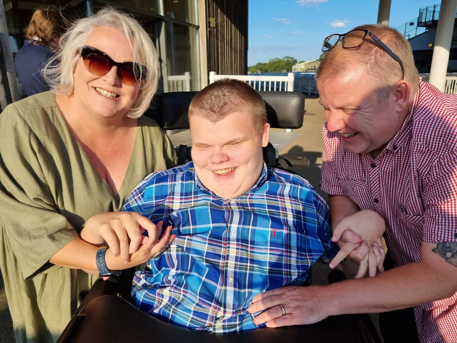 A couple smile alongside their son in a wheelchair, all smiling