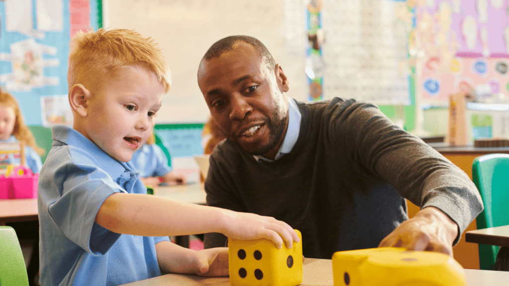 A teacher sitting with a young pupil playing with large dice