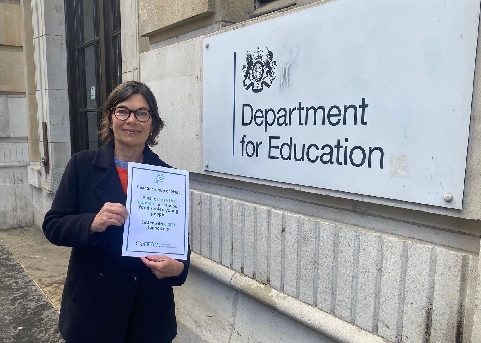 A woman stands outside the Department for Education building holding a letter addressed to the Secretary of State, requesting action for disabled children’s transport and showing support from 6,200 people.