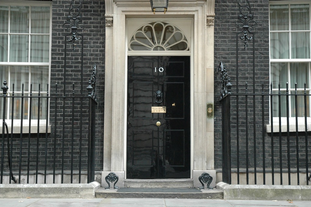 A black door with the number 10 on it, set in a brick building with two windows and black railings on either side.
