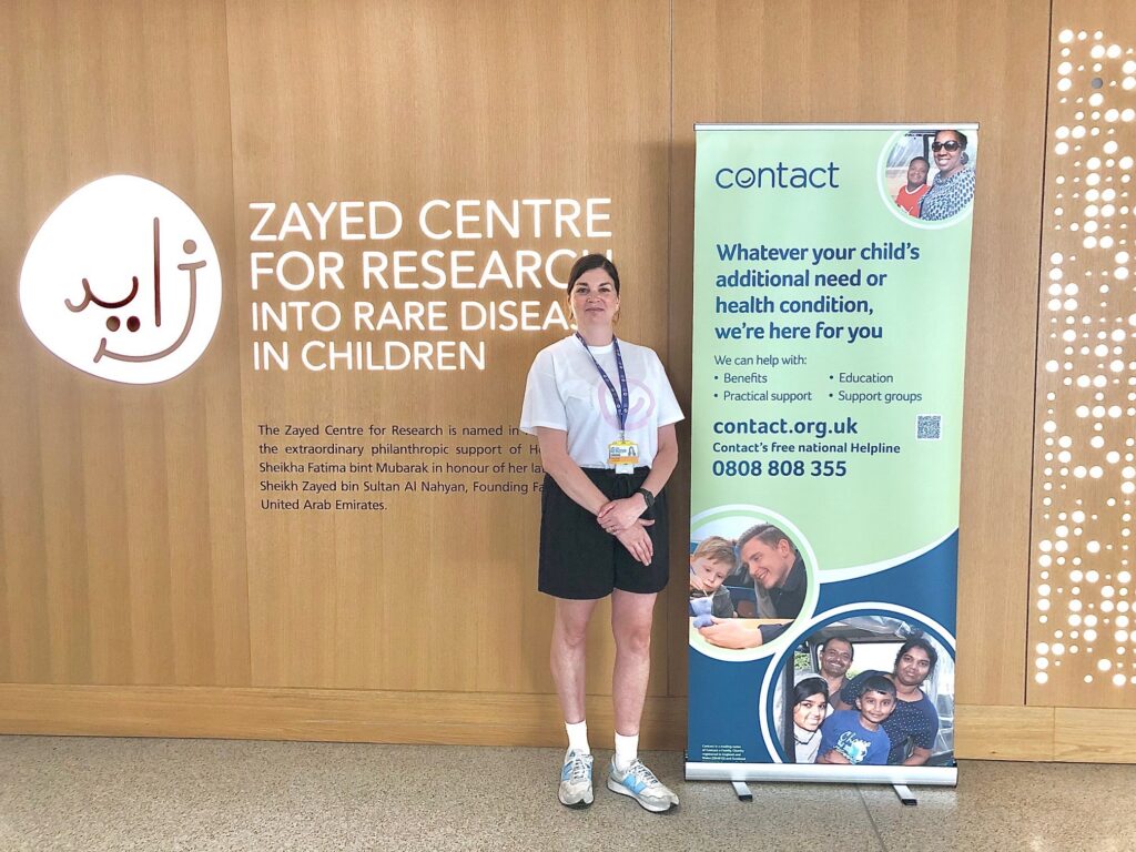 A person stands next to a “Contact” information banner at the Zayed Centre for Research into Rare Disease in Children, with a wooden wall and Centre logo in the background.